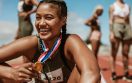 Female runner with a gold medal sitting on track. Running race winner sitting on track with athletes in background.