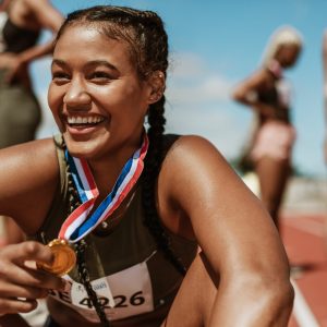 Female runner with a gold medal sitting on track. Running race winner sitting on track with athletes in background.