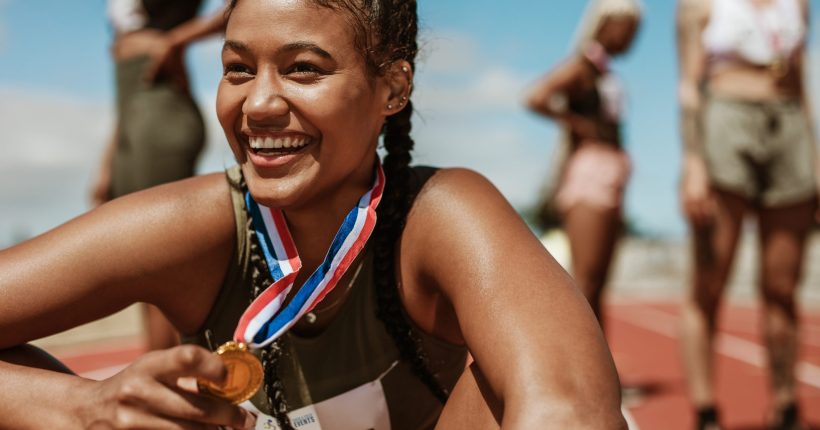 Female runner with a gold medal sitting on track. Running race winner sitting on track with athletes in background.